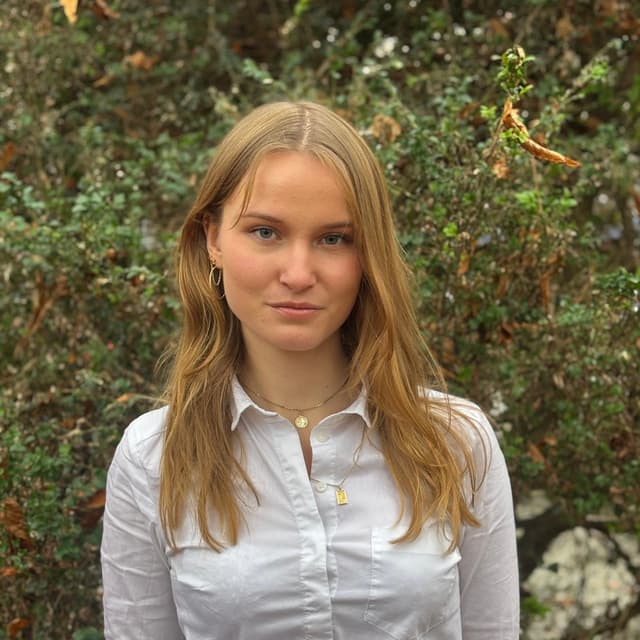 Martine Lecloux steht vor einer Hecke und lächelt in die Kamera.